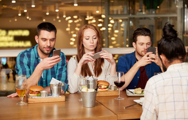 leisure, technology, lifestyle and people concept - friends with smartphones dining at restaurant