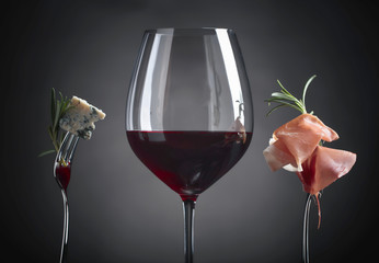 Glass of red wine with blue cheese, rosemary and prosciutto.