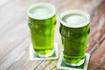 st patricks day, holidays and celebration concept - two glasses of green beer on wooden table