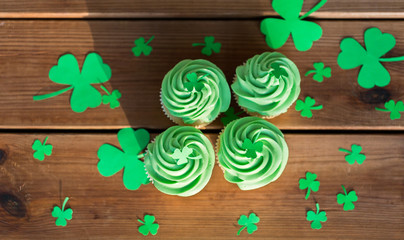 st patricks day, food and holidays concept - green cupcakes and shamrock on wooden table top view