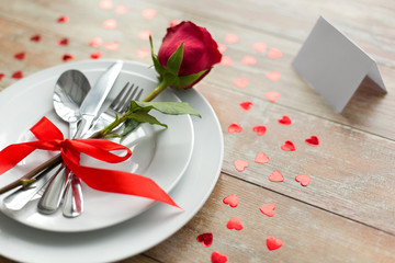 valentines day, table setting and romantic dinner concept - close up of red rose flower on set of dishes with cutlery, hearts and blank place card