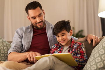family, childhood, fatherhood, leisure and people concept - happy smiling father and little son reading book on sofa at home - Powered by Adobe