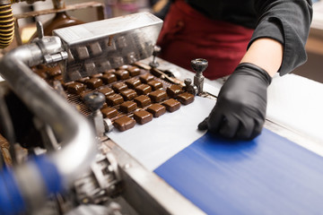 production, candy shop and people concept - confectioner making candies by chocolate coating machine at confectionery