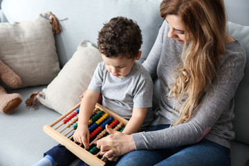 Young mother with cute little son playing with abacus at home
