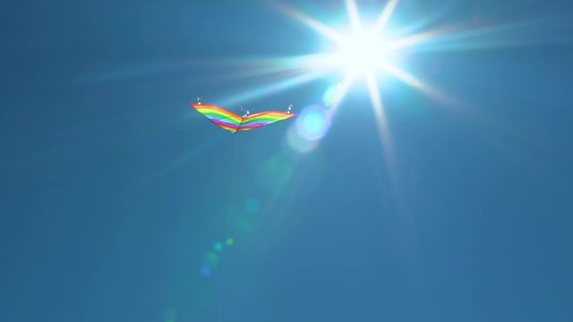 A colored kite in the blue sky. Slowed-down shooting of a kite developing against a blue sky and white clouds
