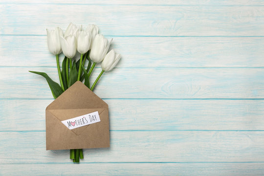 A bouquet of white tulips with a love note and envelope on blue wooden boards . Mother's day