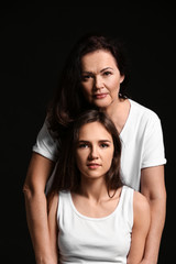 Portrait of young woman with her mother on dark background