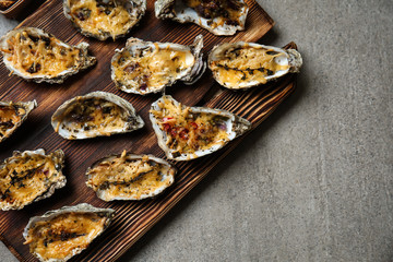 Wooden board with tasty baked oysters on grey table