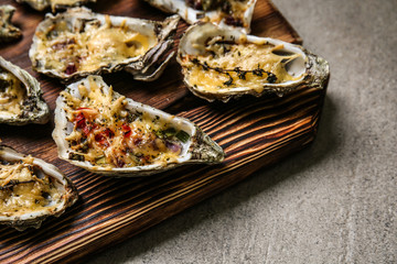 Wooden board with tasty baked oysters on grey table