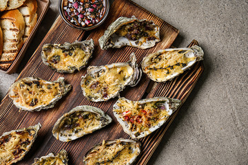 Wooden board with tasty baked oysters on grey table