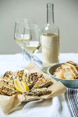 Tasty baked oysters with grilled bread and white wine on table