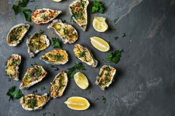 Tasty baked oysters with lemon and herbs on dark background