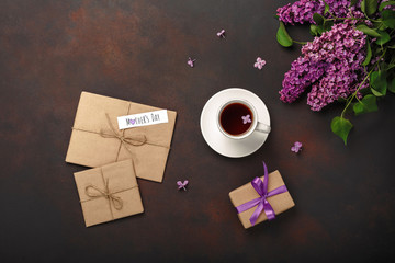A bouquet of lilacs with cup of tea, gift box, craft envelope, a love note on rusty background ....