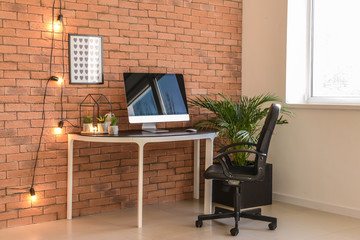 Stylish workplace with modern computer near brick wall