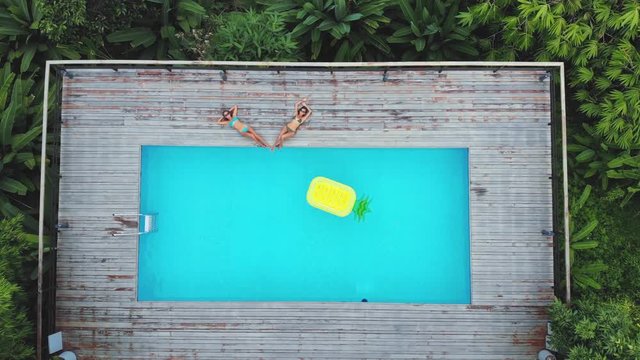 AERIAL. Drone view of two women lying at the swimming pool. Inflatable mattress in swimming pool.