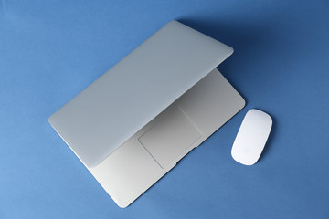 Modern laptop and PC mouse on color background