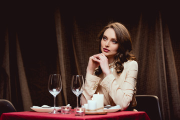 beautiful pensive woman sitting at table and waiting for someone in restaurant