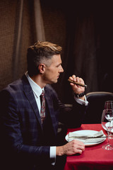 handsome man in formal wear smoking cigar in restaurant