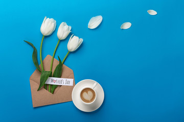 A bouquet of white tulips and a cup of coffee with a love note on a blue background . Mother's day