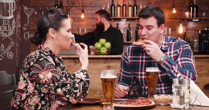 Beautiful couple is dinning in vintage pub or restaurant. There is a hipster bartender in the background at the counter