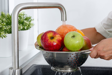 A woman washes fruits by running tap water in the kitchen.