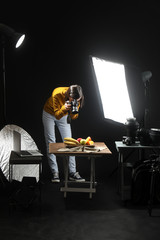 Young woman taking picture of tasty fruits in professional photo studio