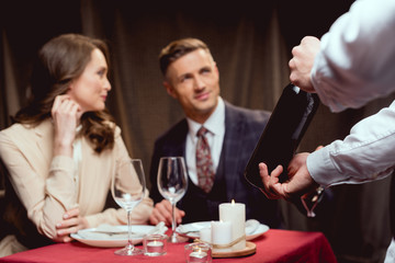 selective focus of waiter showing bottle of wine to beautiful couple during romantic date in restaurant
