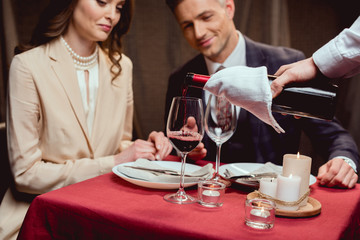 waiter pouring red wine while couple having romantic date in restaurant