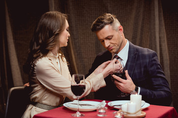 woman adjusting tie of handsome man during romantic date in restaurant