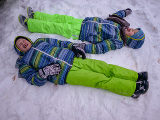 Two happy children in warm winter clothes are playing with falling snow in park. Beautiful winter, mild weather