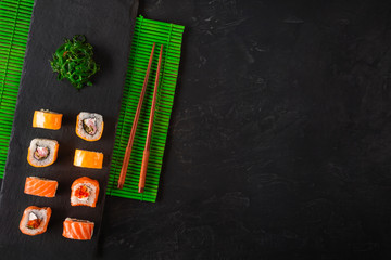 Japanese sushi chopsticks over soy sauce bowl, rice on black stone background. Top view with copy space