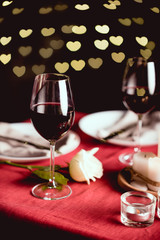 selective focus of red wine glasses with heart shaped bokeh and table setting on background
