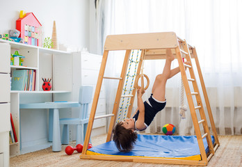 little girl performs gymnastic exercises on a wooden home sports complex
