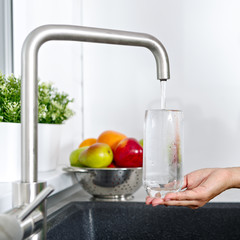 The girl fills a glass with water from a water tap in the kitchen.