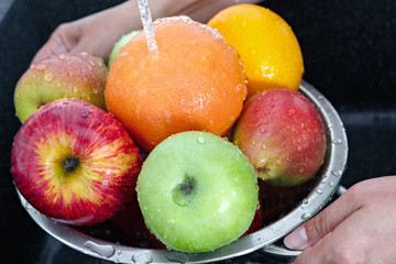 A woman washes fruits by running tap water in the kitchen.