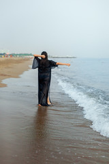 girl in a bathing suit and a black cape walks on the sand, the sea, the beach, the rear view. life style
