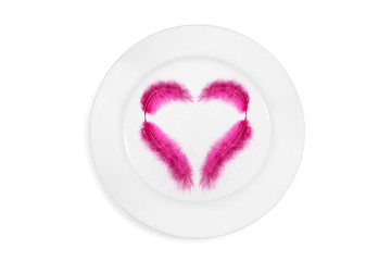 Top view on  a plate with pink feather in the heart shape on a white background. Concept of healthy and light food. Isolated