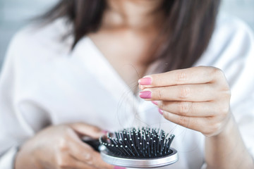 closeup woman having problem with hair loss hand holding hair from hairbrush 