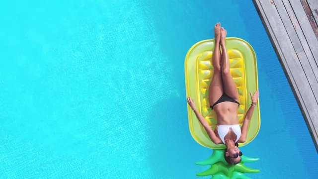 Aerial view of woman on pineapple shaped inflatable mattress in swimming pool.