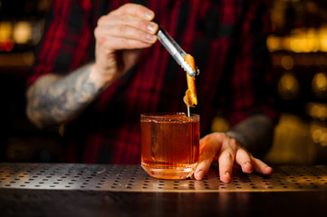 Bartender adding to a Old Fashioned cocktail orange zest