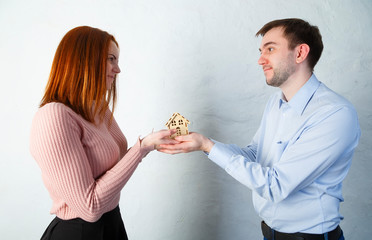 hands of young couple, man and woman hold wooden toy house. The concept of private housing, real estate purchase concept, mortgage