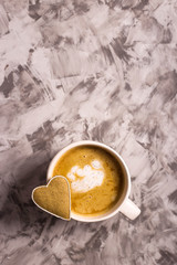 Homemade gingerbread cookie in the shape of a heart with a white outline on a cappuccino cup on a gray background. Valentine's day concept. Minimalism. Background