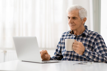 Happy mature man relaxing at home and using laptop