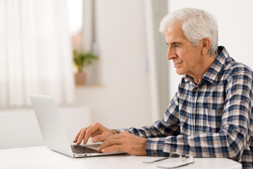 Serious mature man relaxing at home and using laptop