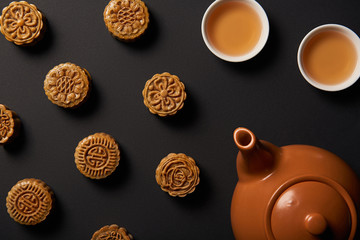 top view of mooncakes, tea pot and cups isolated on black