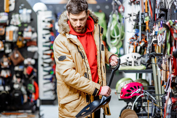 Fototapeta na wymiar Man in winter jacket choosing mountaineer equipment holding snow shovel in the sports shop