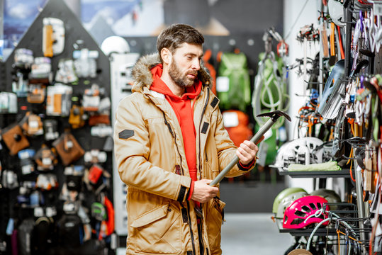 Man in winter jacket choosing mountaineer equipment holding ice axe in the sports shop