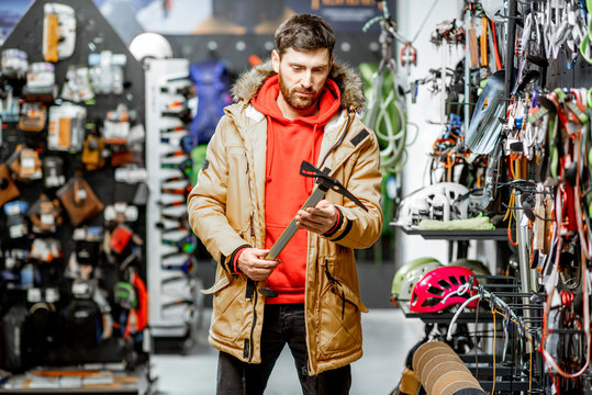 Man in winter jacket choosing mountaineer equipment holding ice axe in the sports shop