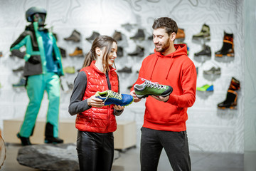 Man and woman choosing shoes for hiking standing in the modern sports shop with beautiful showcase...