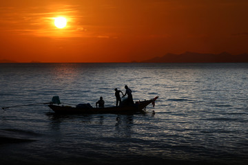 Local fishermen on a long-tail boat in the sea at sunset